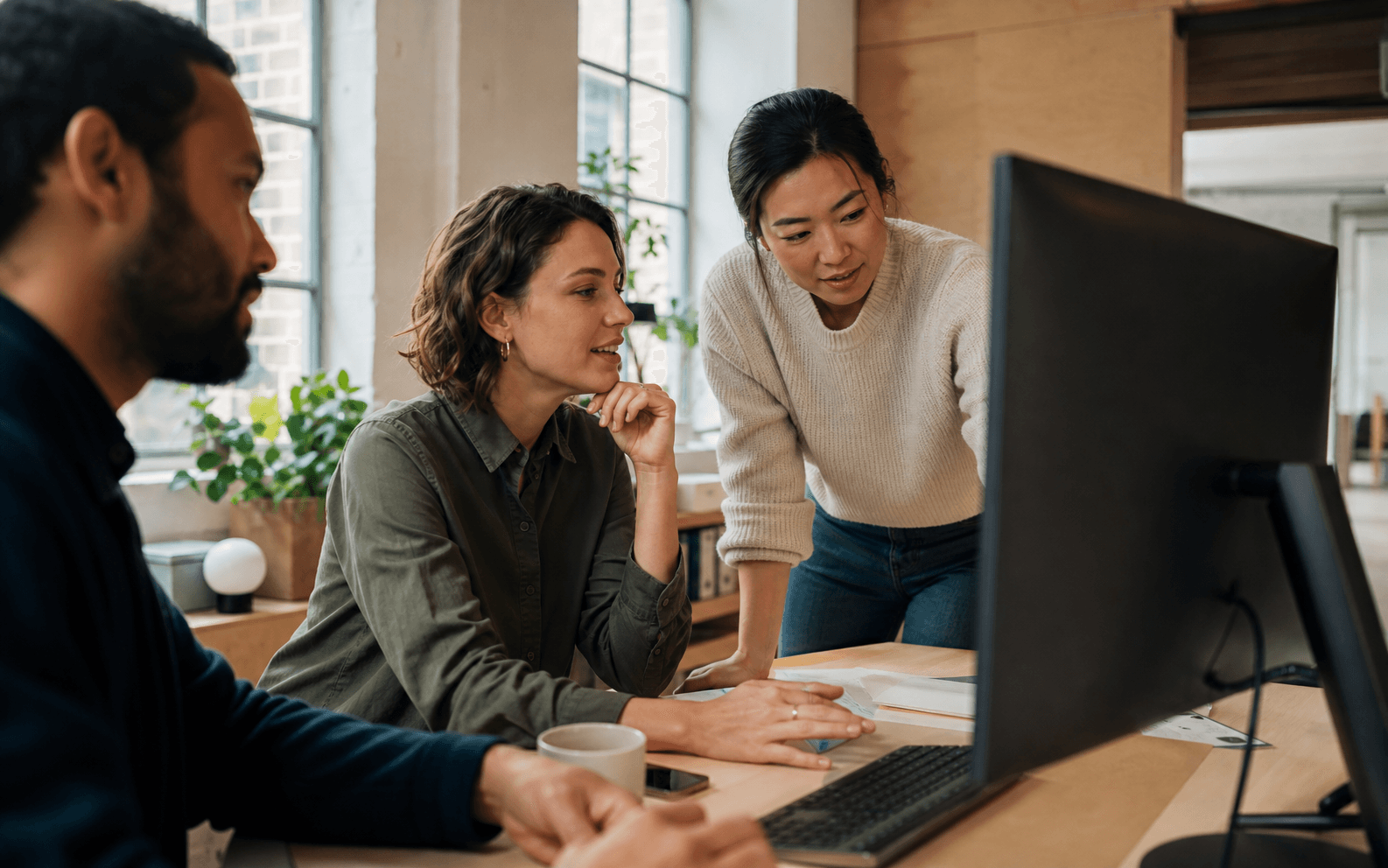 Three colleagues reviewing work together in a sunlit studio
